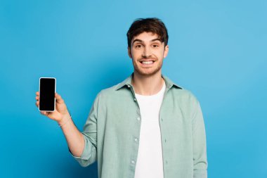 Mutlu genç adam mavi ekranlı akıllı telefon gösteriyor.