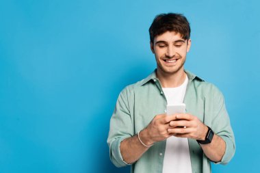 Neşeli genç adam mavi telefonda akıllı telefonla konuşuyor.