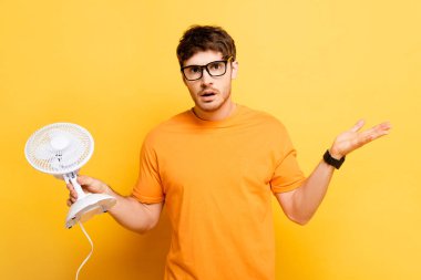 Elektrikli vantilatör tutan ve sarı renkte omuz silken bir adamın cesareti kırılmış.