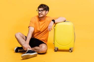 Yaz tatili için seyahat çantasının yanında oturan mutlu turist. 