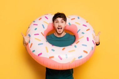 Heyecanlı ve ağzı açık bir adam elinde şişme donutla ayakta duruyor. 