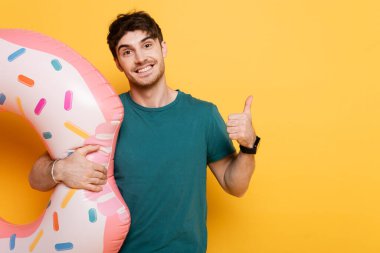 Gülümseyen adam başparmağını gösterirken elinde şişirilebilir donut, sarıda duruyordu. 
