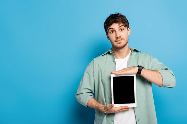 handsome young man showing digital tablet with blank screen on blue