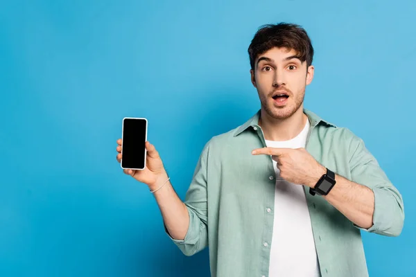 Joven Sorprendido Apuntando Teléfono Inteligente Con Pantalla Blanco Azul —  Fotos de Stock