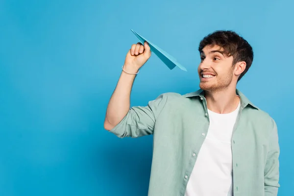 Cheerful Young Man Throwing Paper Plane While Looking Away Blue — Stock Photo, Image