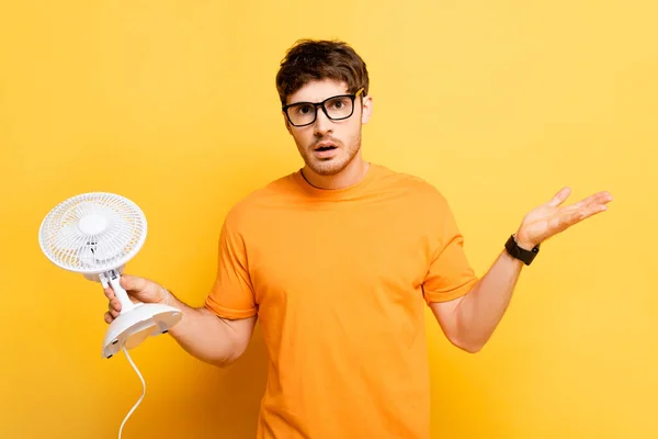 Homem Desencorajado Segurando Ventilador Elétrico Mostrando Gesto Encolher Ombros Amarelo — Fotografia de Stock