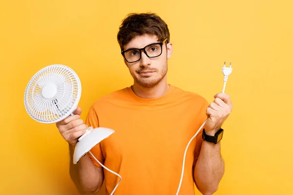 Zklamaný Mladý Muž Drží Elektrický Ventilátor Při Pohledu Kameru Žluté — Stock fotografie