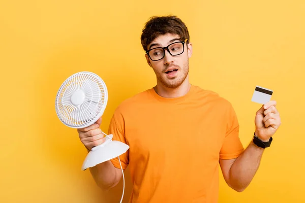 Thoughtful Young Man Holding Electric Fan Credit Card Yellow — Stock Photo, Image