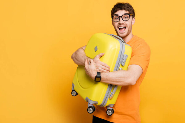 возбужденный мужчина турист держит чемодан для летних каникул на желтый
 