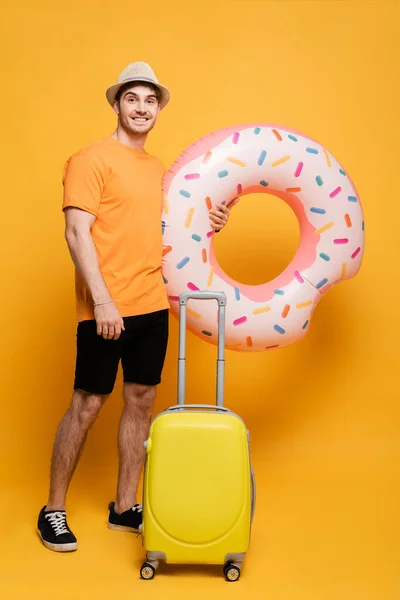 戴着帽子的快乐男人 带着手提箱和充气甜甜圈 准备在黄色的夏天度假 — 图库照片