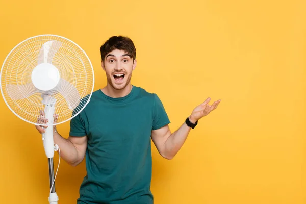 Excited Young Man Gesturing Holding Electric Fan Yellow — Stock Photo, Image