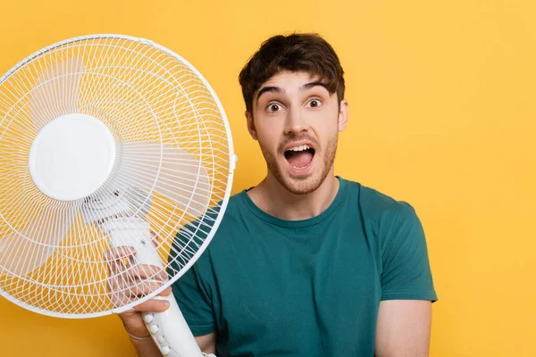 Překvapený Mladý Muž Drží Elektrický Ventilátor Žluté — Stock fotografie