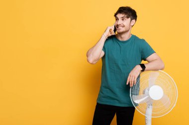 Sarı fanın yanında dururken cep telefonuyla konuşan gülümseyen adam.     