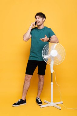 Sarı fanın yanında duran mutlu adam cep telefonuyla konuşuyor.     