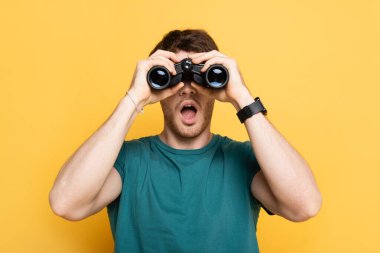 young shocked man looking through binoculars on yellow clipart