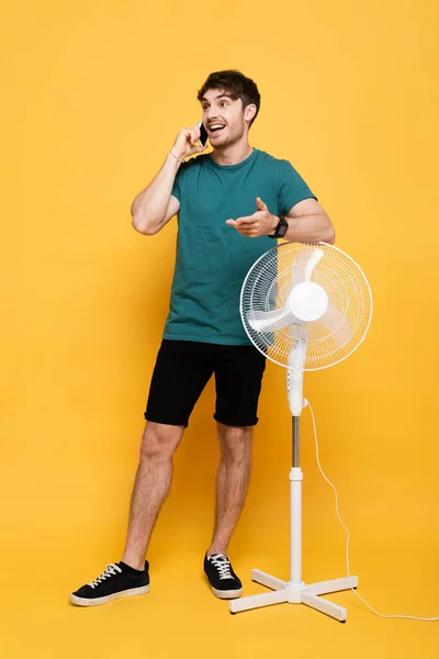 Šťastný Muž Mluví Mobilu Zatímco Stojí Blízkosti Elektrického Ventilátoru Žluté — Stock fotografie