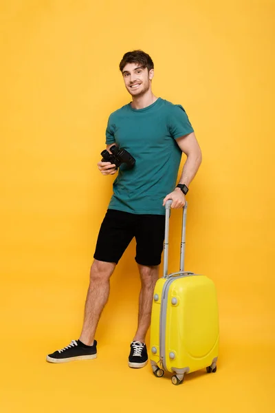黄色の夏休みの準備ができているスーツケースと双眼鏡を持つ幸せな男 — ストック写真