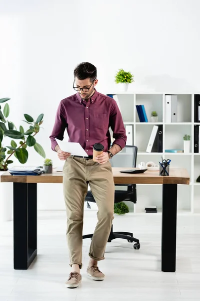 Joven Hombre Negocios Leyendo Documento Sosteniendo Café Para Cerca Escritorio — Foto de Stock