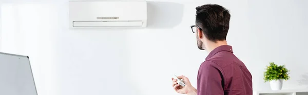 リモコンでオフィスのエアコンをオンにするビジネスマンの水平イメージ — ストック写真