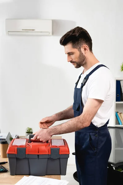 Gutaussehender Reparateur Öffnet Werkzeugkiste Während Der Nähe Einer Defekten Klimaanlage — Stockfoto