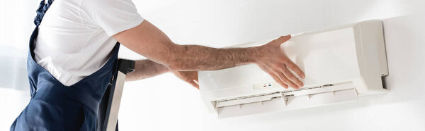 cropped view of repairman fixing air conditioner on white wall