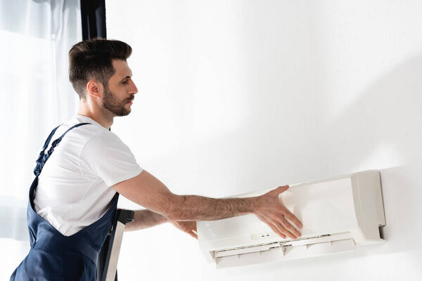 young repairman opening air conditioner fixed on while wall