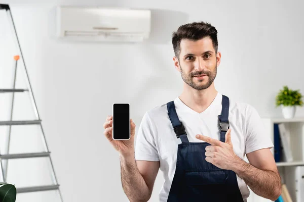 Lächelnder Werkstattmitarbeiter Zeigt Auf Smartphone Mit Leerem Bildschirm Neben Klimaanlage — Stockfoto