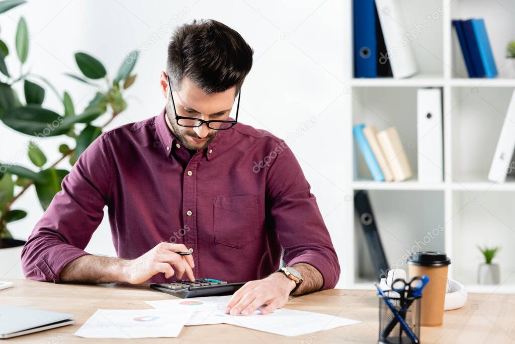 concentrated businessman using calculator near papers and coffee to go 