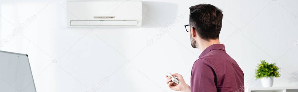 horizontal image of businessman switching on air conditioner in office with remote controller