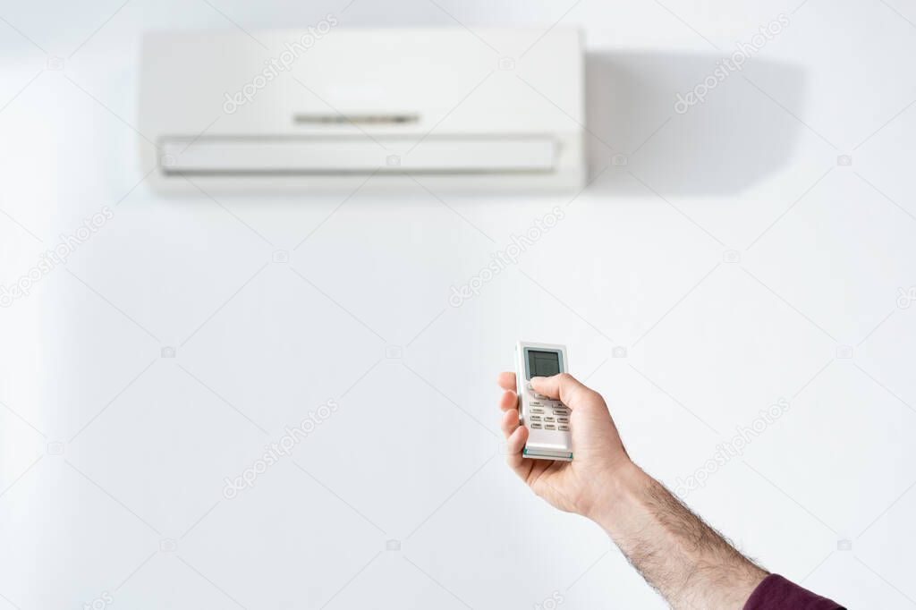 cropped view of businessman switching on air conditioner in office with remote controller