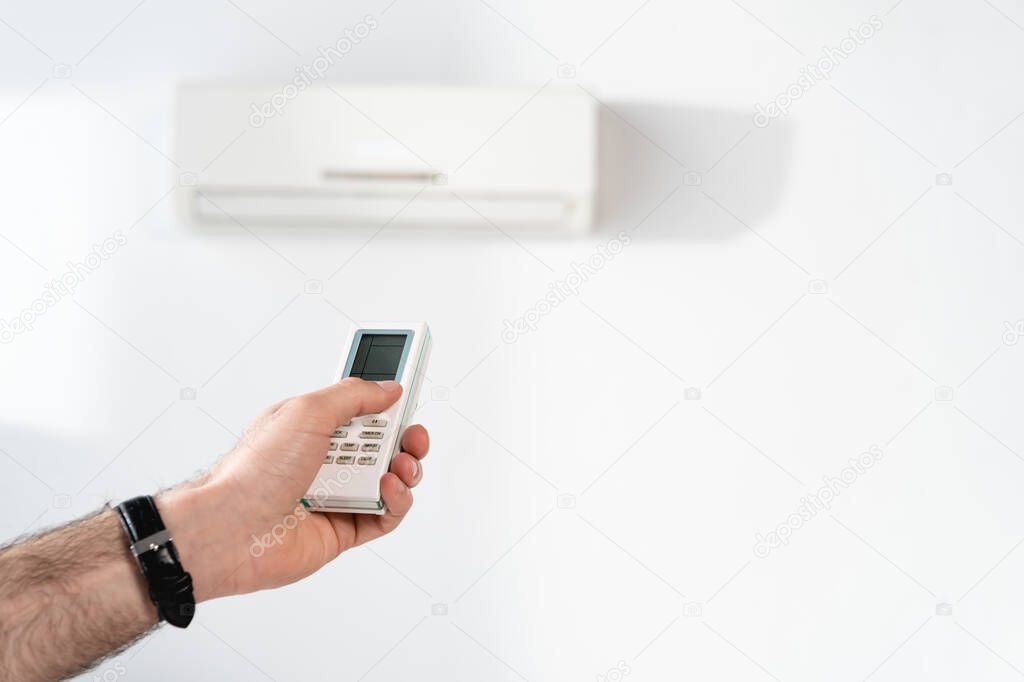 cropped view of businessman switching on air conditioner with remote controller