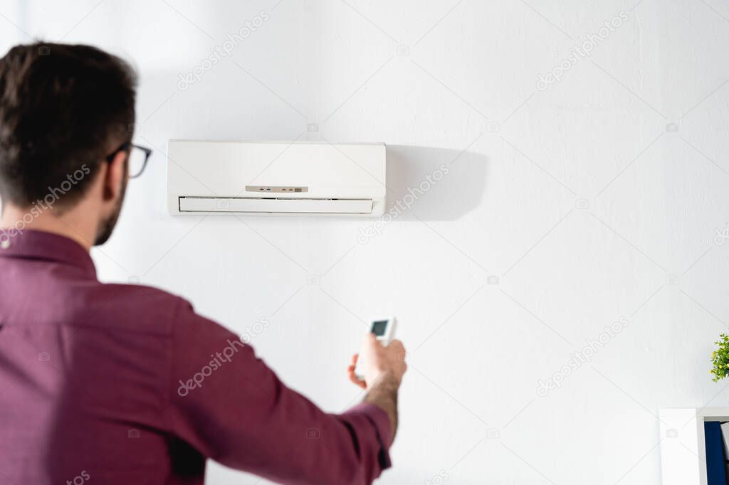 back view of businessman switching on air conditioner with remote controller