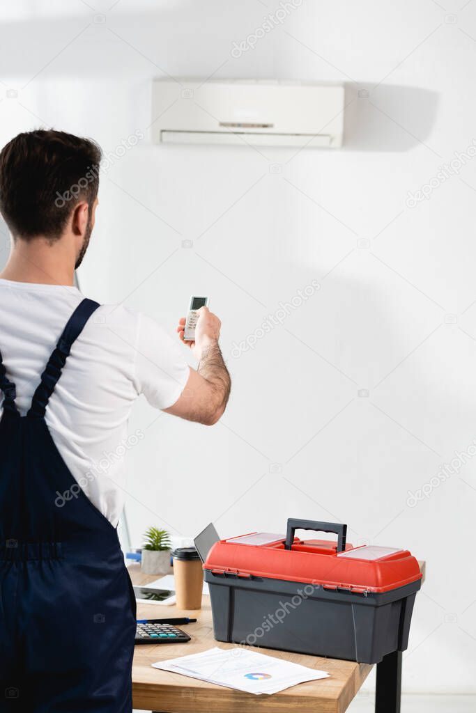 back view of repairman near toolbox holding air conditioner remote controller