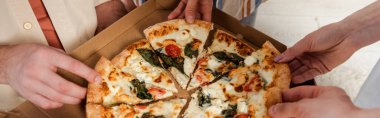 Arkadaşların evde lezzetli pizza parçalarını tuttukları panoramik bir fotoğraf.