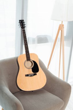 Oturma odasındaki pencerenin yanındaki koltukta akustik gitar.