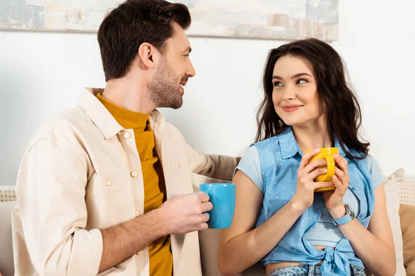 Leende Man Håller Kopp Kaffe Och Tittar Vacker Flickvän Hemma — Stockfoto