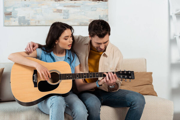 Man teaching girlfriend to playing acoustic guitar in living room