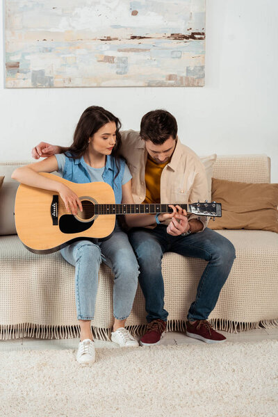 Young couple playing acoustic guitar together in living room