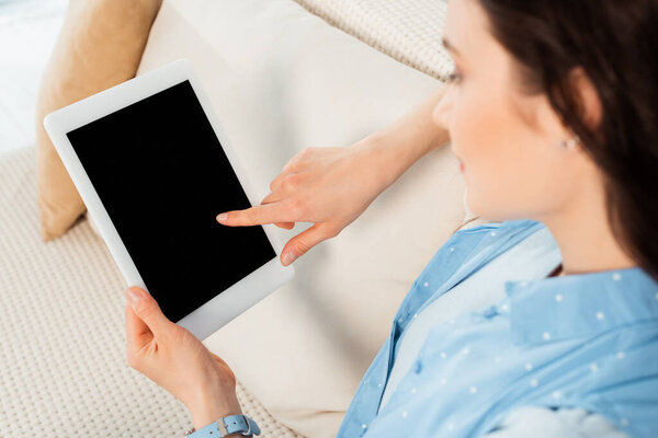 Selective focus of young woman using digital tablet with blank screen on couch 
