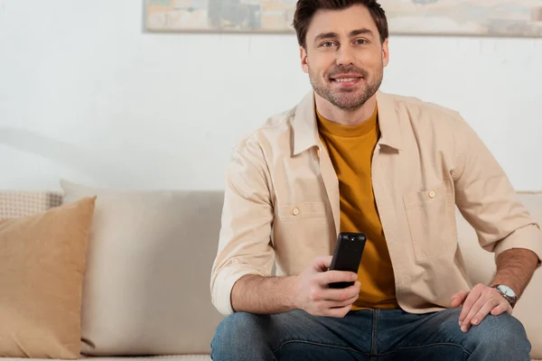 Smiling man holding remote controller while watching tv at home