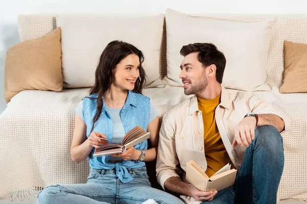 Casal Jovem Sorrindo Para Outro Enquanto Lia Livros Casa — Fotografia de Stock