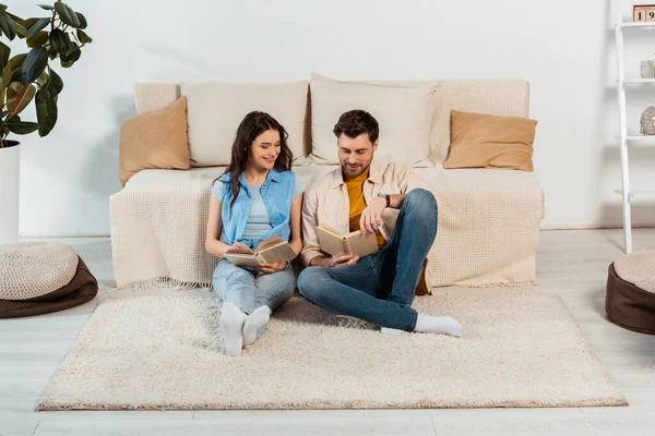 Glimlachende Vrouw Boek Lezen Buurt Van Knappe Vriend Vloer Thuis — Stockfoto