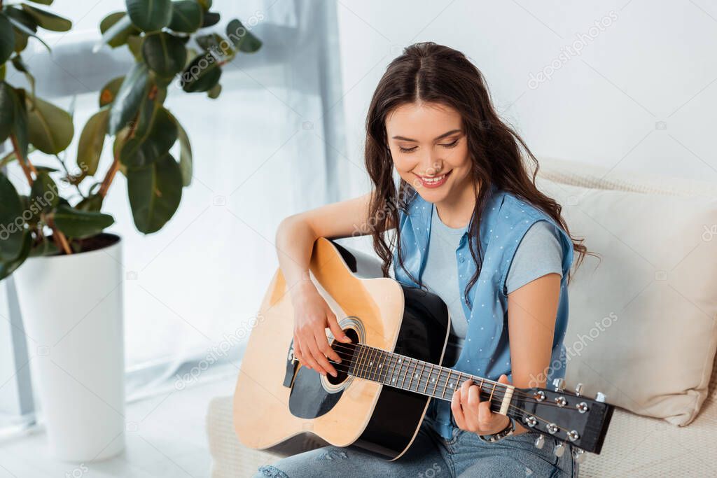 Beautiful smiling woman playing acoustic guitar in living room