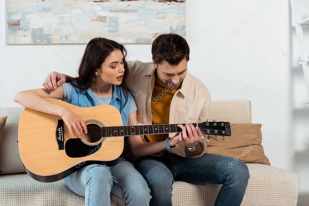 Man teaching girlfriend to playing acoustic guitar in living room