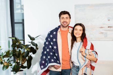 Yakışıklı adam Amerikan bayrağına sarılmış gülümseyen kız arkadaşına sarılıyor. 