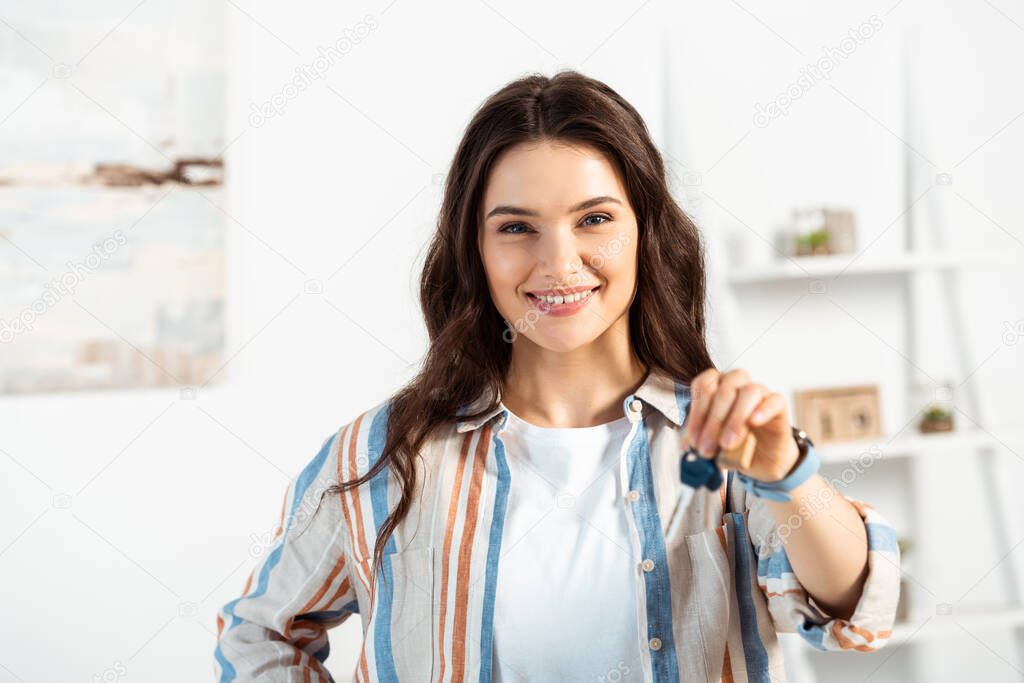 Selective focus of smiling woman holding keys of new house in living room