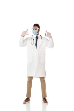 Güvenlik gözlüklü ve maskeli doktor beyaz arka planda kan örnekleri olan test tüpleri tutuyor.