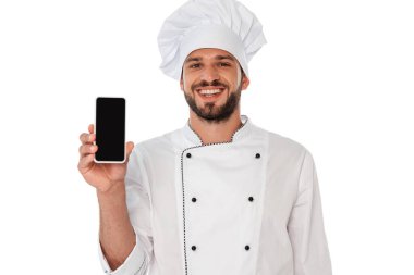 Smiling chef in uniform showing smartphone with blank screen isolated on white clipart