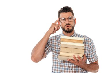 Concentrated nerd in eyeglasses holding books and pointing with finger at head isolated on white clipart