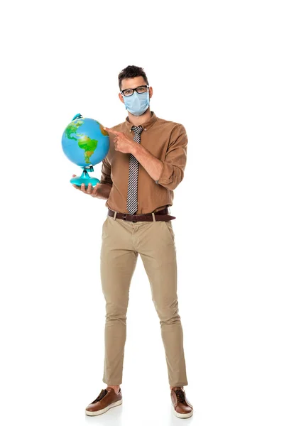 戴医疗面罩的老师 手指指向白色背景的地球仪 — 图库照片